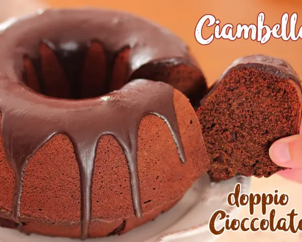 Ciambellone al cioccolato con glassa fondente. Una fetta viene sollevata, mostrando la consistenza soffice e il ricco colore del dolce.