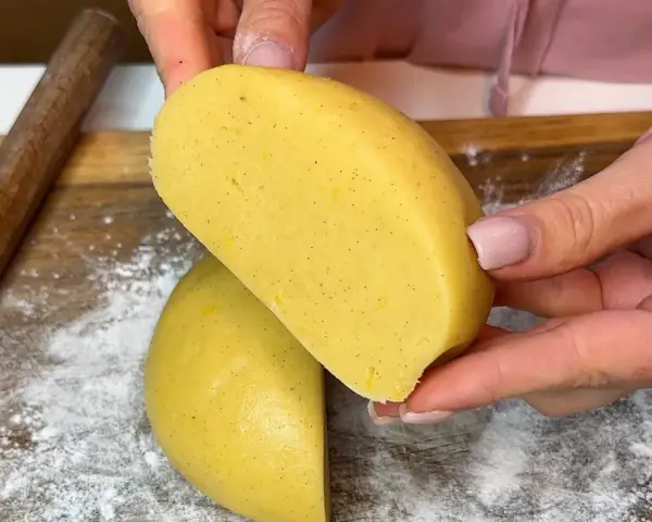 Mani che tengono un impasto giallo, profumato alla vaniglia, pronto per diventare una deliziosa pasta frolla senza burro.