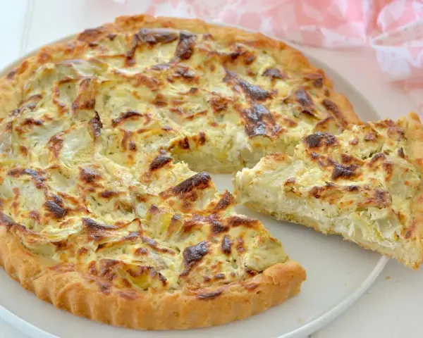 Una deliziosa torta salata con carciofi, dorata e invitante, con una fetta appena tagliata che mostra il ripieno cremoso.