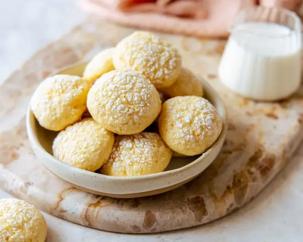 Biscotti da inzuppo spolverati di zucchero a velo in una ciotola, pronti per essere gustati con un bicchierino di latte.