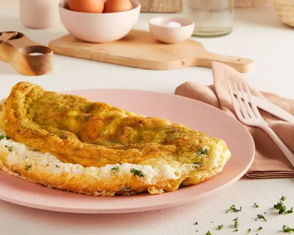 Frittata soffice e dorata, preparata in friggitrice ad aria, servita su un piatto rosa con erbe fresche.