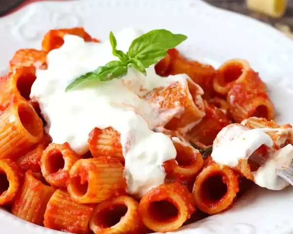 Rigatoni al sugo rosso con abbondante stracciatella cremosa e una fogliolina di basilico.