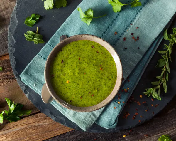 Una ciotola di vibrante salsa verde senza uovo, guarnita con peperoncino rosso tritato e erbe fresche. Perfetta per accompagnare i tuoi piatti preferiti.