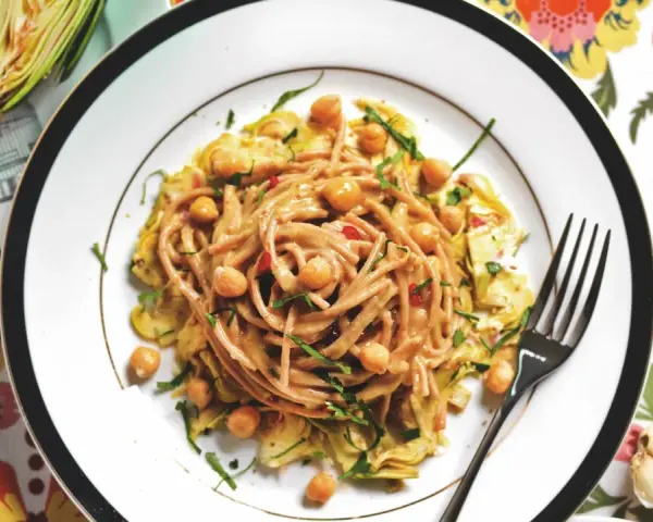 Un piatto invitante di pasta con carciofi alla siciliana, arricchito da ceci e erbe fresche, su un tovagliolo fiorito.