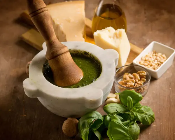 Mortaiolo in marmo con pestello in legno, basilico fresco, pinoli, noci, aglio, parmigiano e olio d'oliva, ingredienti per un autentico pesto di basilico.