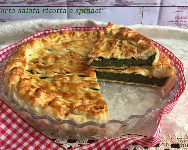 Torta salata ricotta e spinaci dorata e invitante, con una fetta tagliata che mostra il ripieno verde e cremoso.