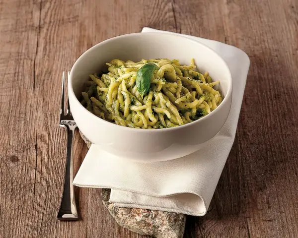 Un piatto invitante di trofie al pesto, guarnito con una foglia di basilico, su un tavolo di legno rustico.