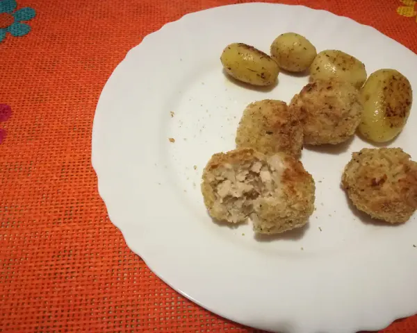 Piatto con polpette di pollo dorate e patate novelle condite. Una polpetta è stata aperta, mostrando l'interno succulento.