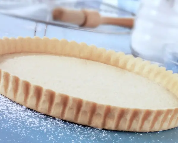 Base per crostata pronta, una deliziosa pasta frolla senza uova, cosparsa di zucchero a velo su un piano blu.