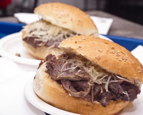 Panino con la milza, un classico street food siciliano, servito su un panino morbido con semi di sesamo e abbondante formaggio grattugiato.
