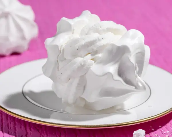 Dolci meringhe bianche, perfette per le tue ricette con albumi, su un piatto con bordo dorato, su sfondo fucsia.