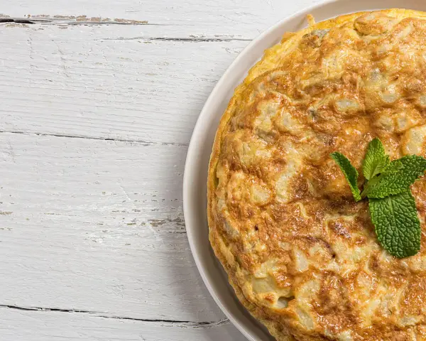 Frittata di cipolle dorata e soffice, guarnita con foglie di menta fresca, su un tavolo di legno bianco.