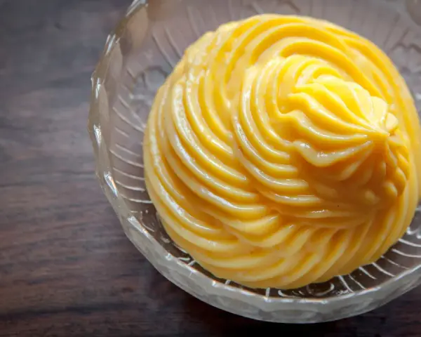 Crema pasticcera ricetta: una deliziosa crema gialla, liscia e lucida, servita in una ciotola di vetro trasparente con decori.