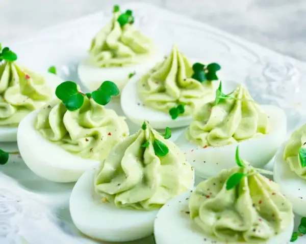 Uova ripiene per Pasqua, guarnite con crema verde e germogli freschi, un antipasto colorato e delizioso.