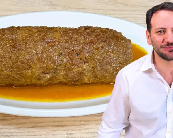 Un uomo sorride accanto a un succulento polpettone in padella, pronto per essere gustato.