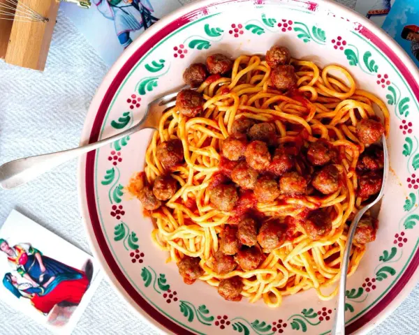 Un piatto di spaghetti alla chitarra con polpettine al sugo, serviti in un piatto decorato.