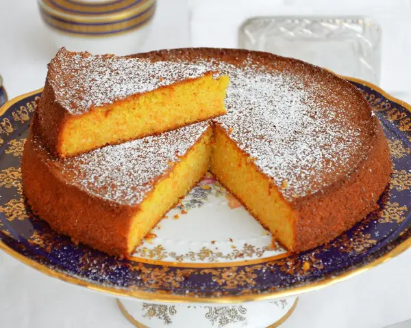 Deliziosa torta carote e mandorle, spolverata di zucchero a velo, servita su un elegante alzata.