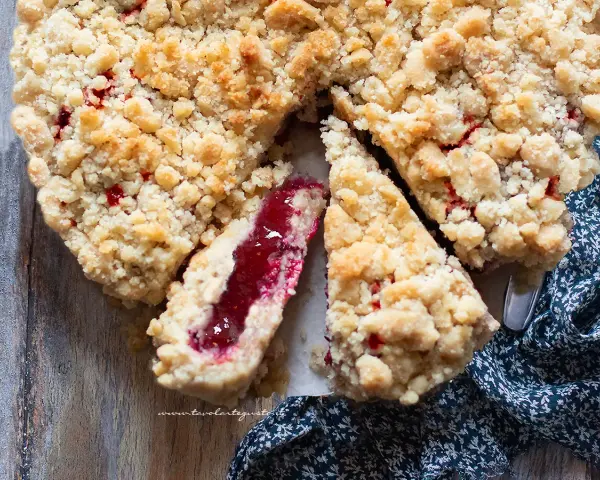 Torta con marmellata, con crosta friabile e ripieno rosso brillante. Una fetta mostra la consistenza succosa.