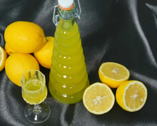 Limoncello fatto in casa: una bottiglia e un bicchierino di liquore giallo brillante, circondati da limoni freschi. La ricetta limoncello 1 litro alcool è pronta per essere gustata.