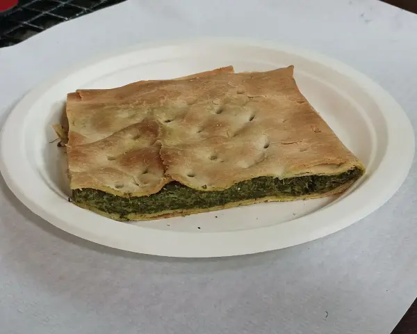Una fetta di torta pasqualina originale genovese, con pasta sfoglia dorata e ripieno verde di spinaci e ricotta, servita su un piatto bianco.