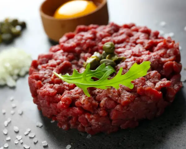 Battuta di fassona cruda, guarnita con capperi e rucola, con tuorlo d'uovo e cipolla tritata sullo sfondo.