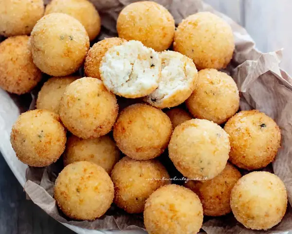 Un cesto pieno di croccanti polpette di ricotta, dorate e invitanti. Una è aperta, mostrando il morbido interno.