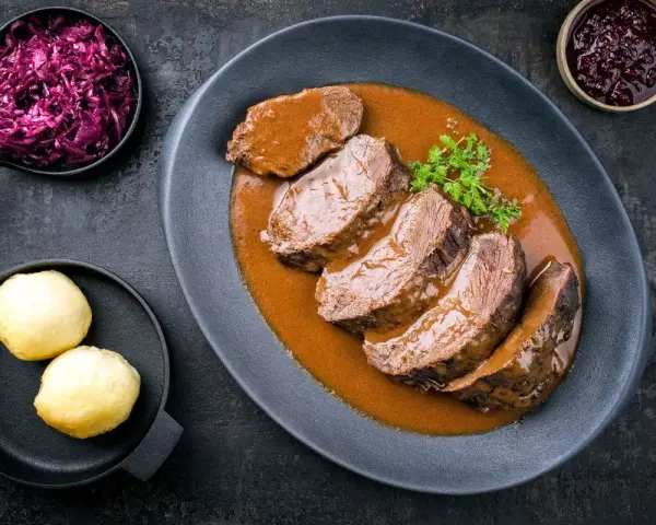 Fette fette di girello di vitello in salsa, accompagnate da cavolo rosso e canederli.