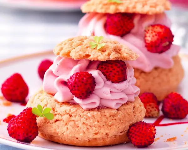 Deliziosa mousse di fragole su bignè, guarnita con fragoline di bosco e foglioline verdi.