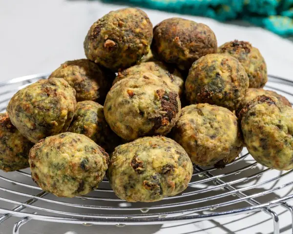 Pile di polpette ricotta e spinaci dorate e appetitose su una griglia metallica.