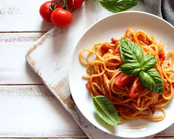 Spaghetti al sugo di pomodoro fresco, guarniti con basilico e pomodorini, su un piatto bianco.