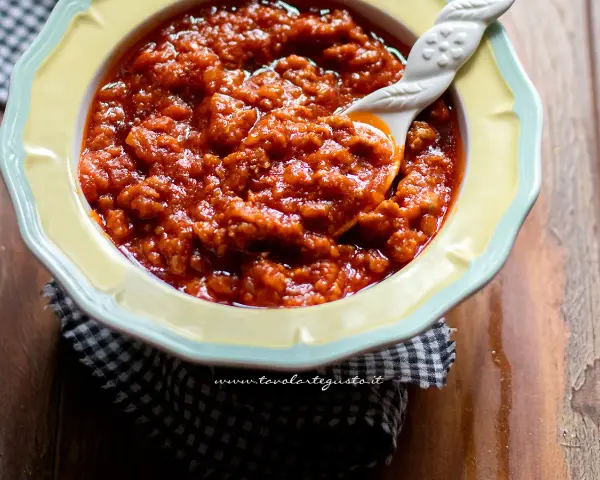 Un invitante sugo con salsiccia, denso e saporito, servito in una ciotola gialla con un cucchiaio decorato.
