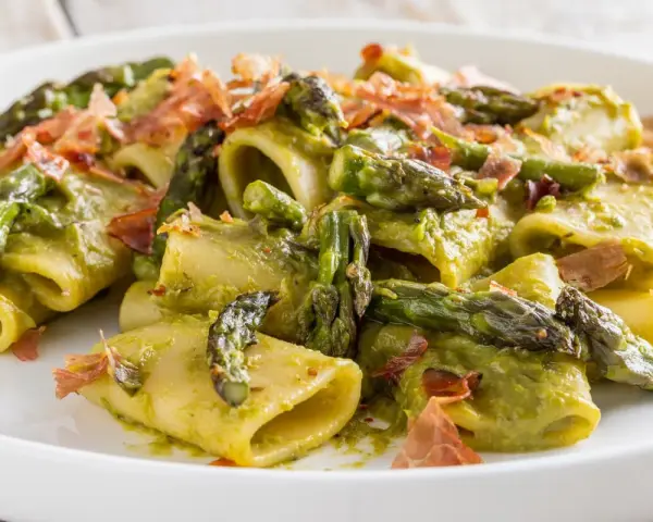 Paccheri conditi con una cremosa salsa verde e asparagi selvatici, guarniti con croccante prosciutto.