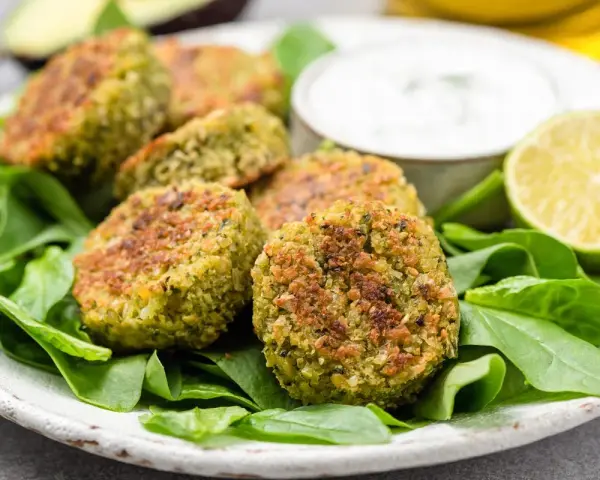 Deliziose polpette di spinaci dorate, servite su un letto di spinacini freschi con salsa e spicchi di lime.
