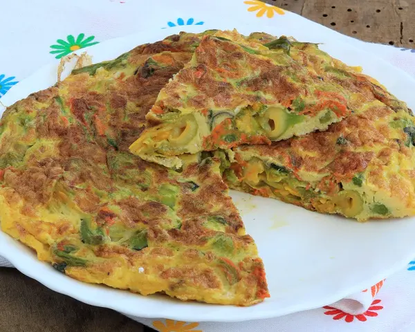 Frittata con fiori di zucca, carote e olive, tagliata a spicchi su un piatto bianco, con un tovagliolo fiorato sullo sfondo.