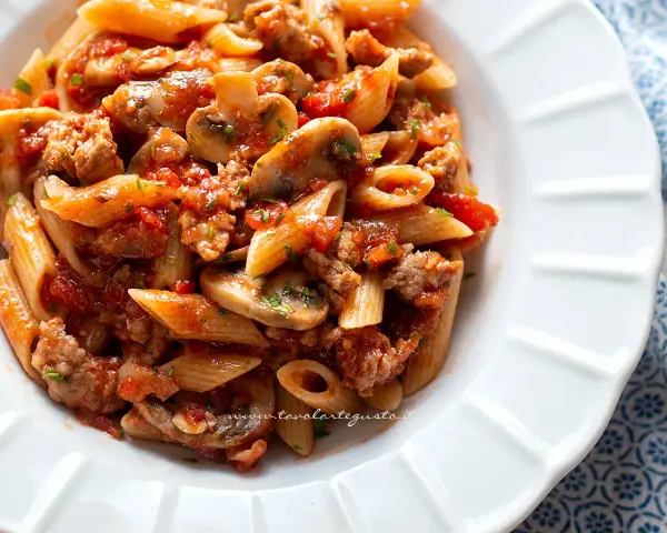 Piatto di pasta alla boscaiola con penne, funghi, salsiccia e pomodoro, condita con prezzemolo fresco.