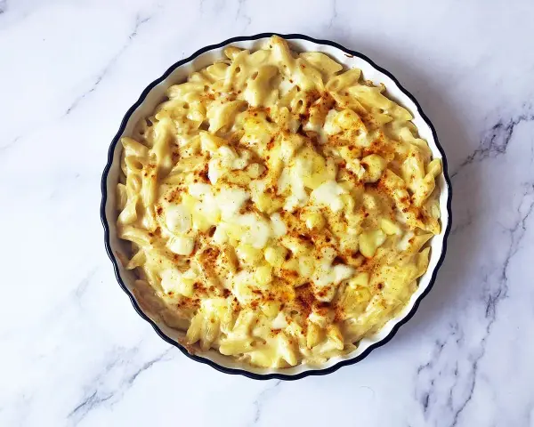 Piatto di mac and cheese fumante, con pasta penne cremosa e formaggio fuso, spolverato con paprika.
