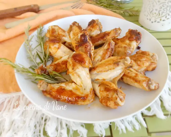A plate of golden-brown, juicy chicken wings garnished with rosemary sprigs.