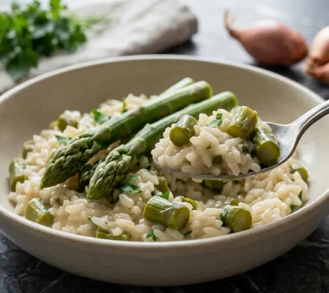 Un cremoso risotto con asparagi freschi, guarnito con prezzemolo tritato. Una forchettata mostra la consistenza perfetta.