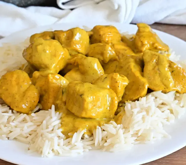 Piatto di riso basmati con saporito pollo al curry, ricoperto da una cremosa salsa gialla.