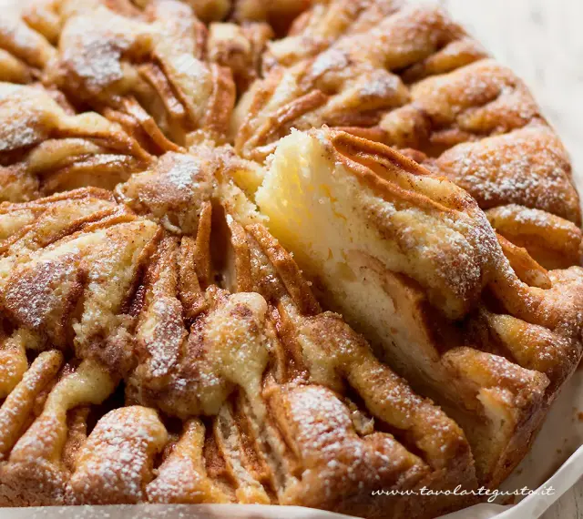 Una deliziosa torta di mele, cosparsa di zucchero a velo, con una fetta appena tolta che rivela la morbidezza dell'impasto e le mele caramellate.
