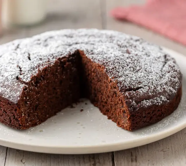 Una deliziosa torta al cioccolato, cosparsa di zucchero a velo, con una fetta mancante su un piatto bianco.