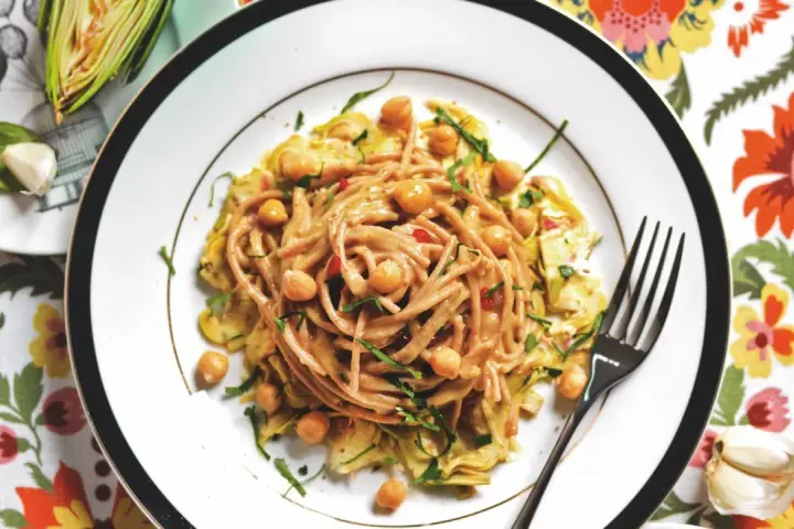 Un piatto invitante di pasta con carciofi alla siciliana, arricchito da ceci e erbe fresche, su un tovagliolo fiorito.