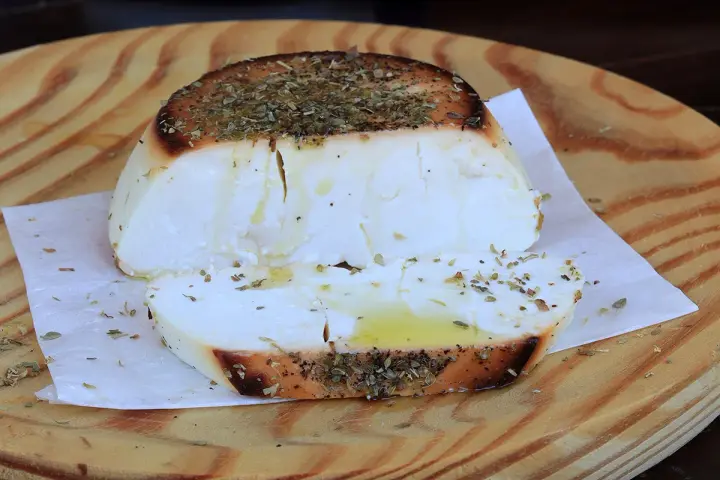 Ricotta al forno dorata e profumata con erbe aromatiche, servita su un tagliere di legno.