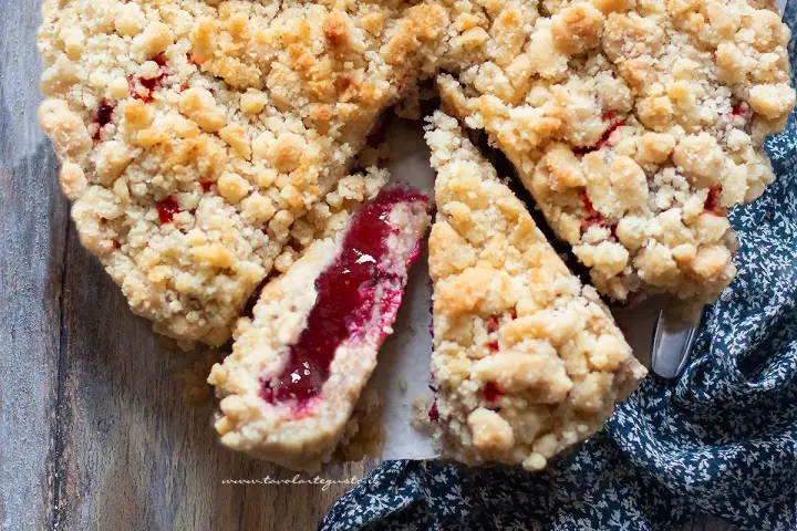 Torta con marmellata, con crosta friabile e ripieno rosso brillante. Una fetta mostra la consistenza succosa.