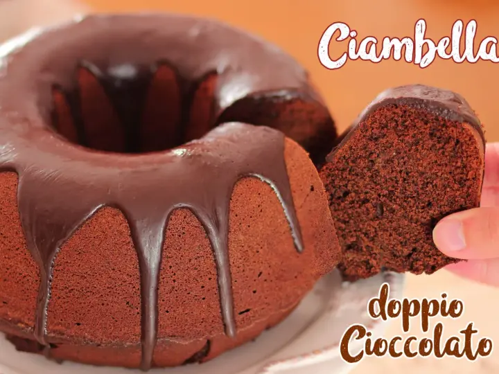 Ciambellone al cioccolato con glassa fondente. Una fetta viene sollevata, mostrando la consistenza soffice e il ricco colore del dolce.
