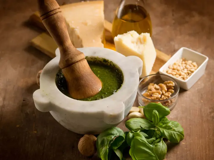 Mortaiolo in marmo con pestello in legno, basilico fresco, pinoli, noci, aglio, parmigiano e olio d'oliva, ingredienti per un autentico pesto di basilico.
