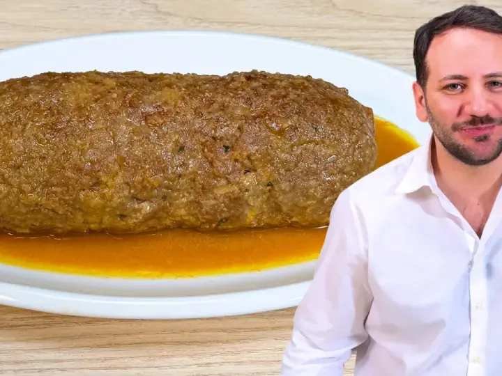 Un uomo sorride accanto a un succulento polpettone in padella, pronto per essere gustato.
