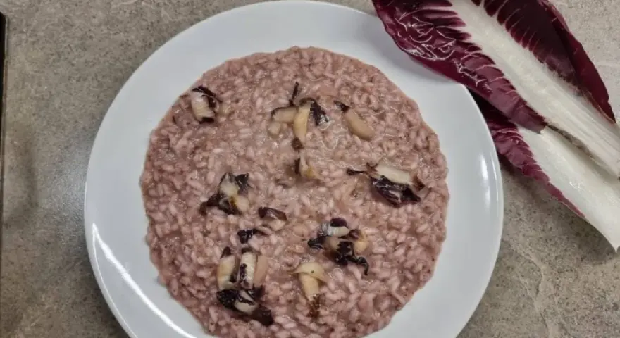 Un cremoso risotto al radicchio, con pezzetti di verdura che spuntano dal riso. Accanto, una foglia di radicchio fresco.