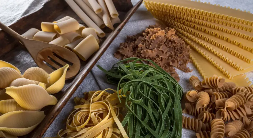 Varietà di pasta cruda, tra cui conchiglioni, paccheri, fettuccine verdi e gialle, lasagne e fusilli, pronte per essere condite con i migliori sughi per pasta.