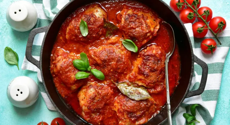 Pollo in umido succulento in padella con pomodoro e basilico, pronto per essere gustato.